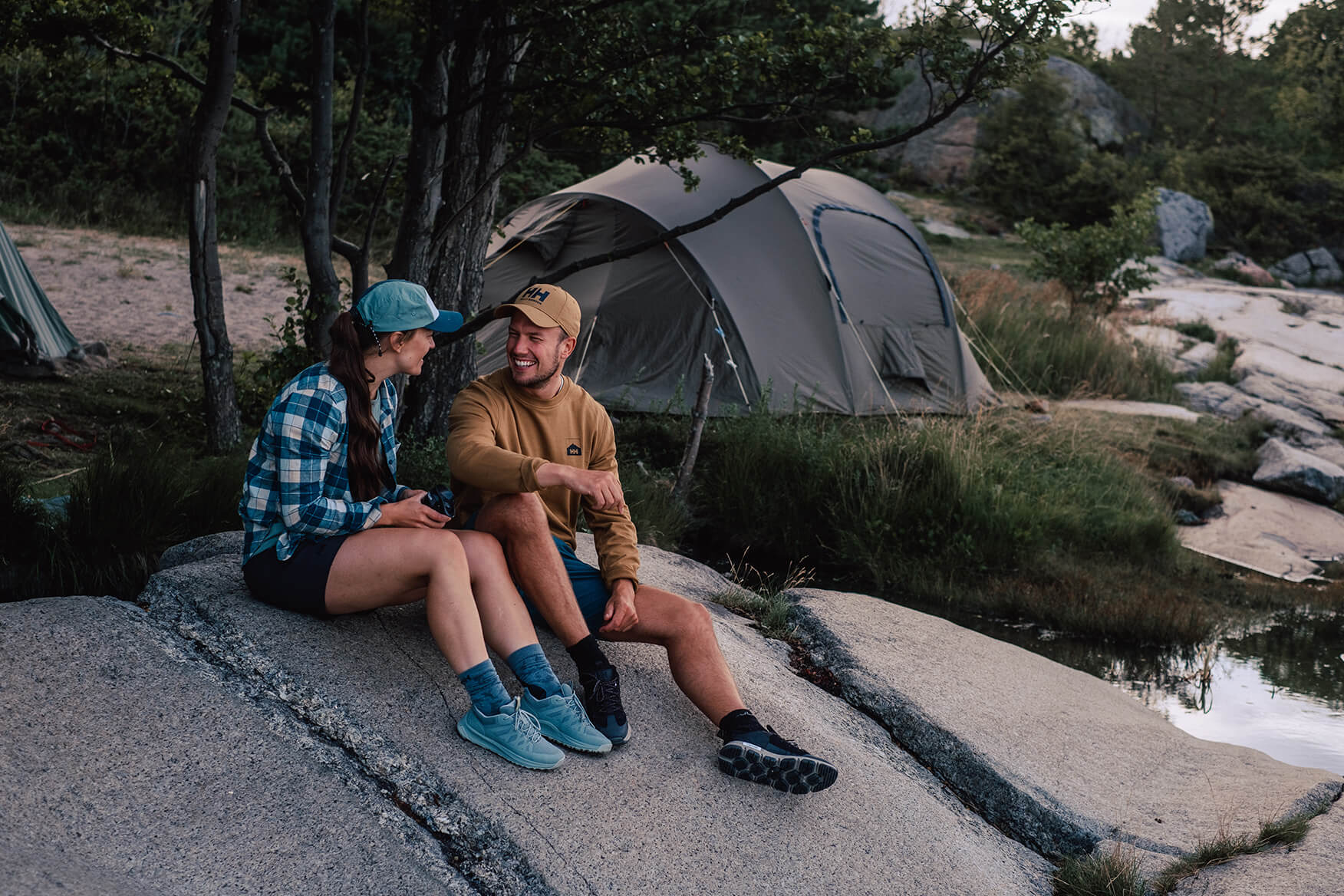 a man and a woman sitting outside a tent in the forest