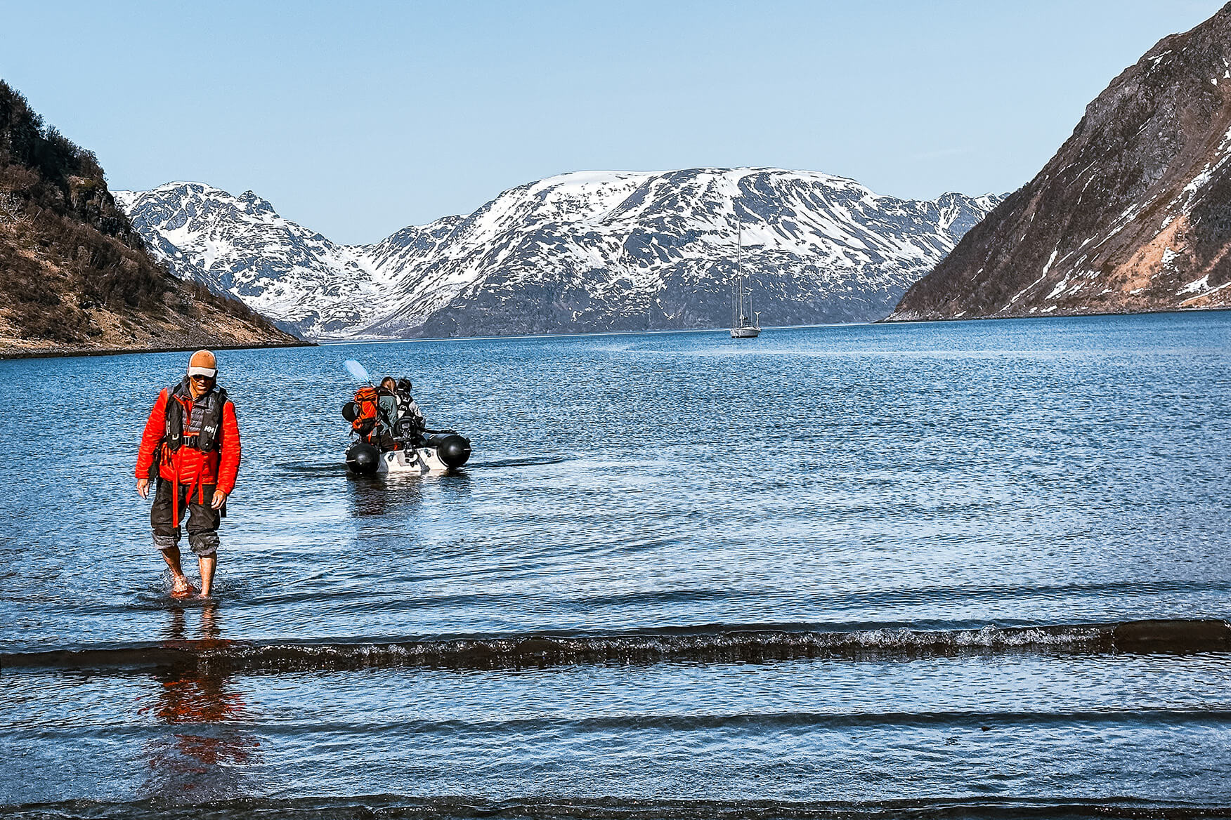 Guide Jordi Tosas wades onto the beach on a sunny morning. The water is ice cold so you'll be happy you brought waterproof rubber boots. Skier wading towards shore on a beach in Finnmark