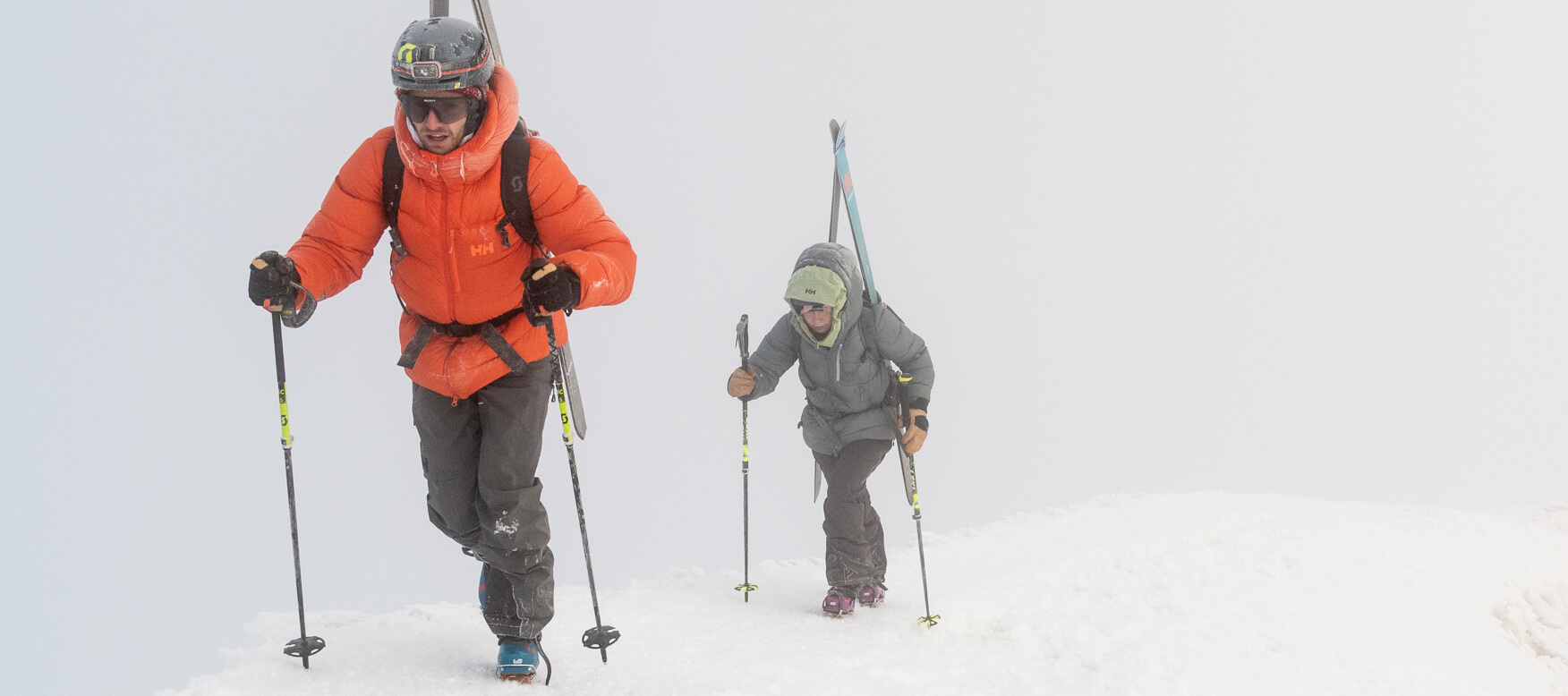 2 men hiking up the mountain with skis on 