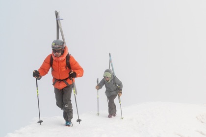 2 men hiking up the mountain with skis on 