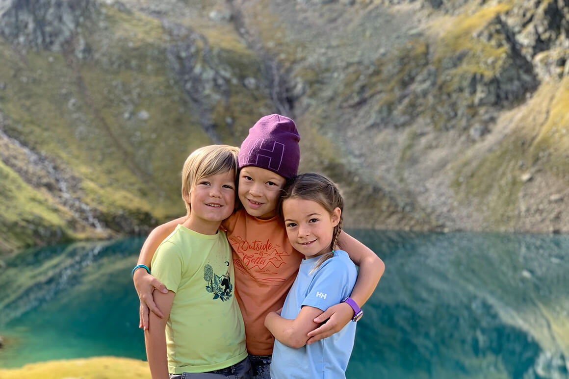 3 kids standing by a lake in the mountains