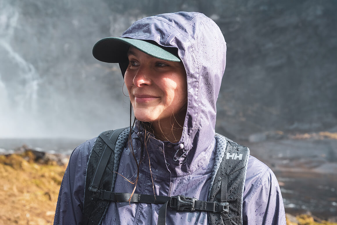 Rain jackets for hiking have different features you need to consider to get the most out of your adventure Woman standing in forrest wearing a purple shell jacket.