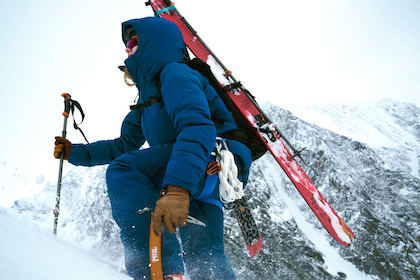 person hiking up the mountain with skiis on their back