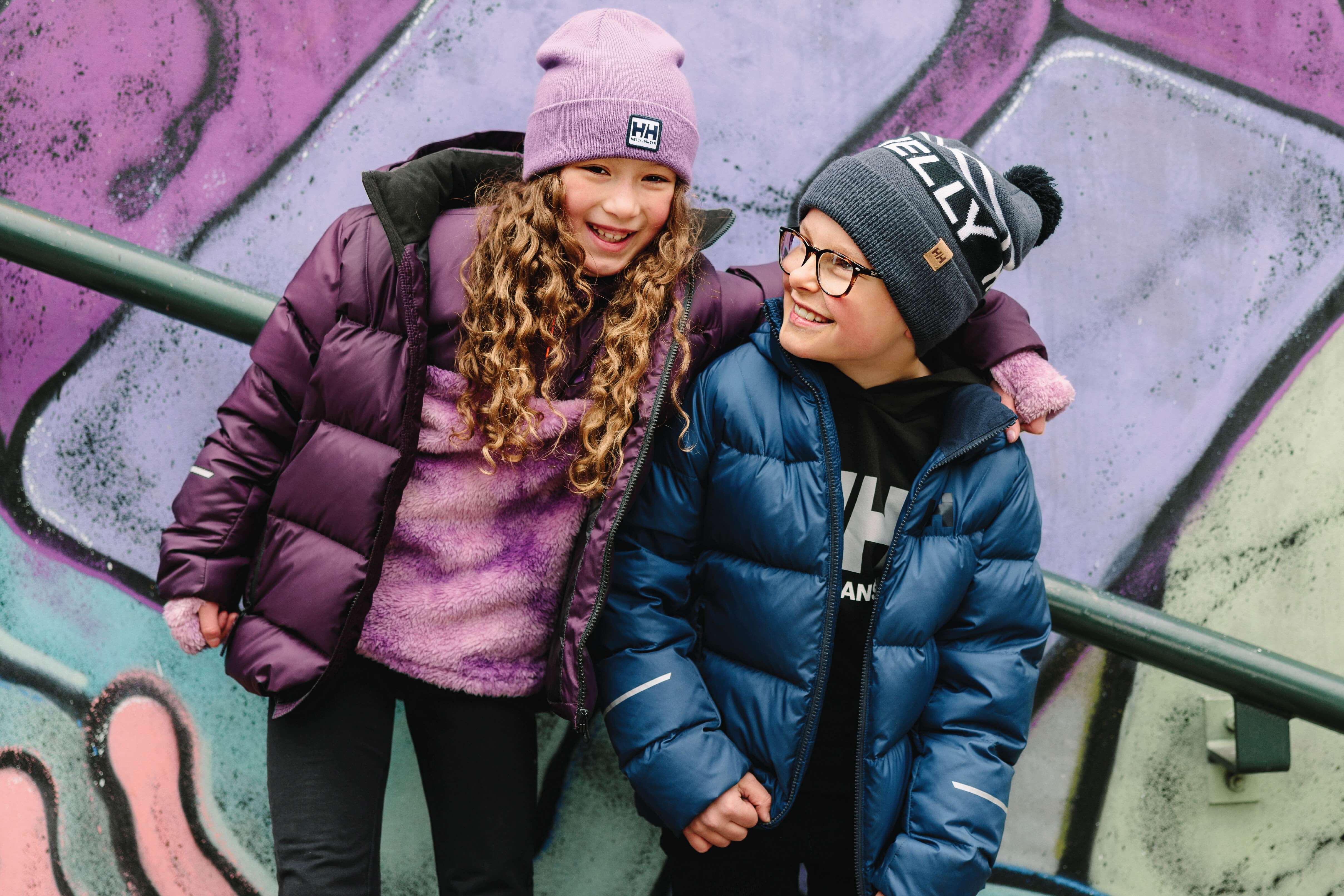 a boy and a girl standing in front of a grafitti wall