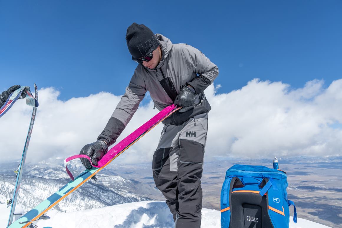 Man on mountaintop removing ski skins to prepare for descent 