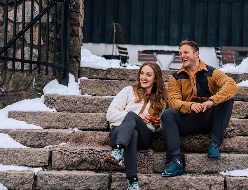 Woman and man sitting on stone stairs outside, laughing, both wearing pile fleece jackets