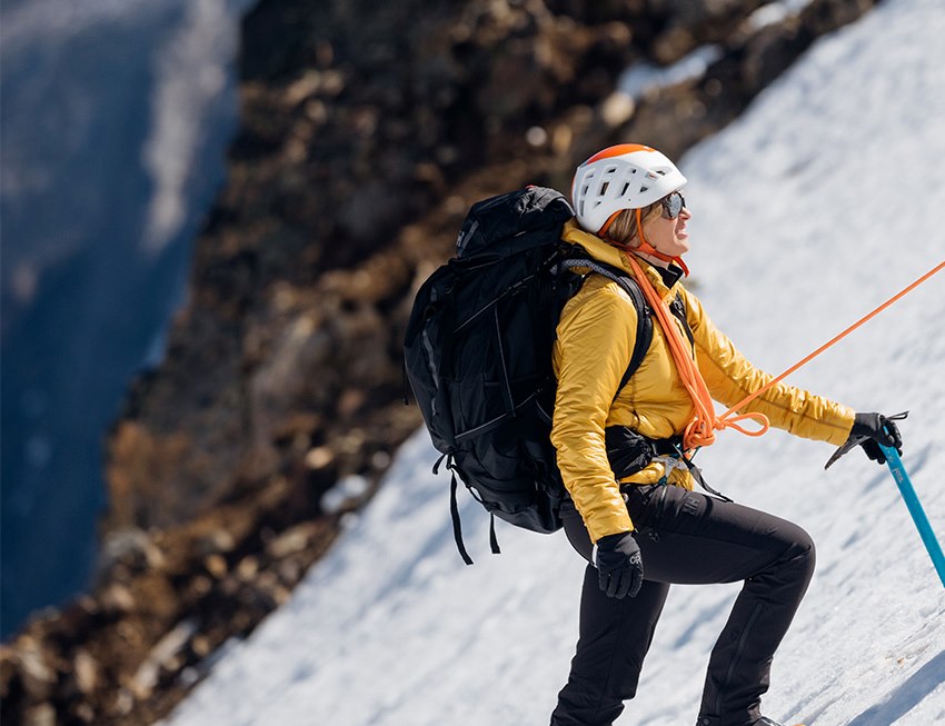 Woman with climbing rope and helmet hiking up a snowy mountain